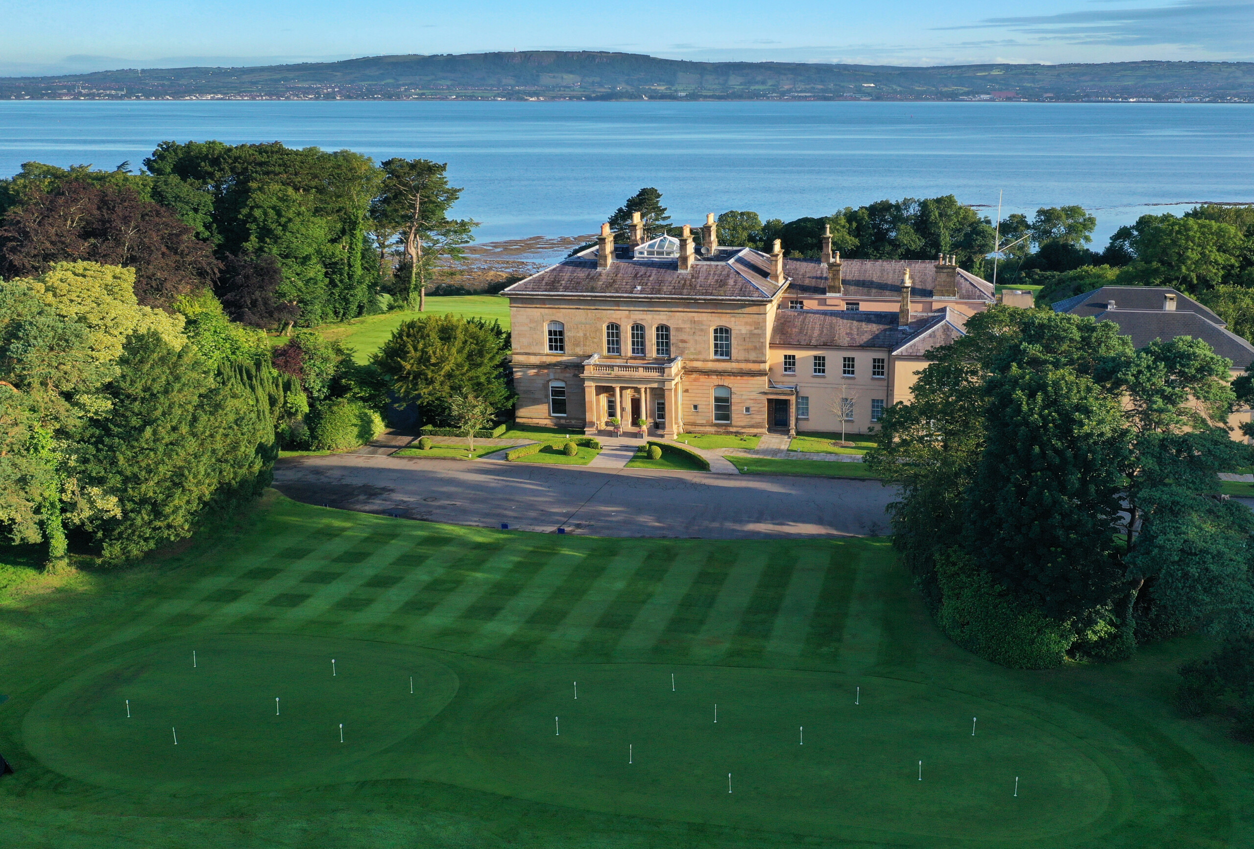 the royal belfast golf club clubhouse surrounded by trees with belfast lough behind it